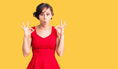 Beautiful young woman with short hair wearing casual style with sleeveless shirt looking surprised and shocked doing ok approval symbol with fingers. crazy expression