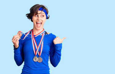 Beautiful young woman with short hair wearing winner medals pointing thumb up to the side smiling happy with open mouth