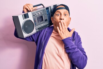 Senior handsome grey-haired modern man listening to music using vintage boombox covering mouth with hand, shocked and afraid for mistake. Surprised expression