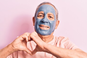 Senior man with grey hair wearing mud mask smiling in love doing heart symbol shape with hands....