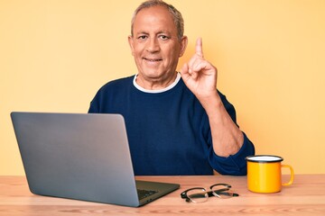 Senior handsome man with gray hair working at the office with laptop surprised with an idea or question pointing finger with happy face, number one