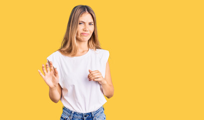 Beautiful caucasian woman with blonde hair wearing casual white tshirt disgusted expression,...