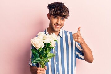 Young hispanic man holding flowers smiling happy and positive, thumb up doing excellent and approval sign