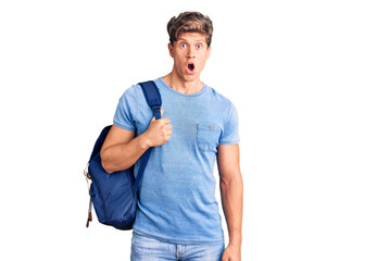 Young handsome man holding student backpack scared and amazed with open mouth for surprise, disbelief face