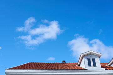 A roof of a house with a clear blue sky and white clouds on a background. Copy space.