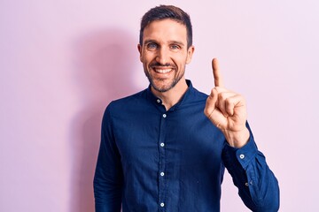 Young handsome man wearing casual shirt standing over isolated pink background smiling with an idea or question pointing finger up with happy face, number one