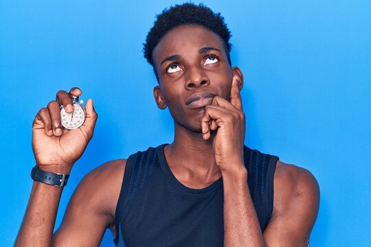 Young african american man holding stopwatch serious face thinking about question with hand on chin, thoughtful about confusing idea