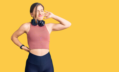 Beautiful caucasian young woman wearing gym clothes and using headphones suffering of neck ache injury, touching neck with hand, muscular pain