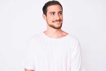 Young handsome man wearing casual white tshirt looking away to side with smile on face, natural expression. laughing confident.