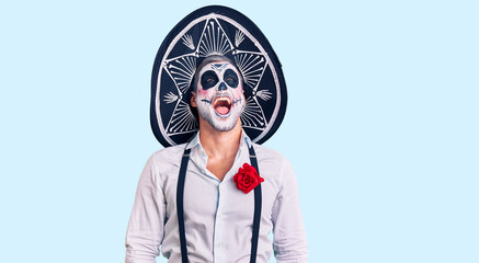 Man wearing day of the dead costume over background angry and mad screaming frustrated and furious,...