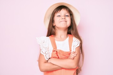 Little caucasian kid girl with long hair wearing spring hat happy face smiling with crossed arms looking at the camera. positive person.