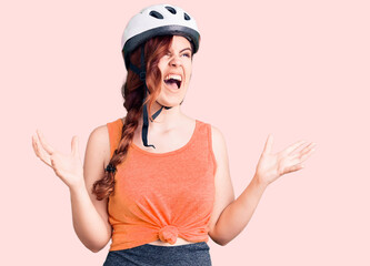 Young beautiful woman wearing bike helmet crazy and mad shouting and yelling with aggressive expression and arms raised. frustration concept.