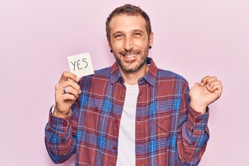 Young handsome man holding yes reminder screaming proud, celebrating victory and success very...