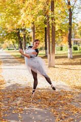 Woman ballerina in a white ballet skirt dancing in pointe shoes in a golden autumn park on dry yellow leaves.