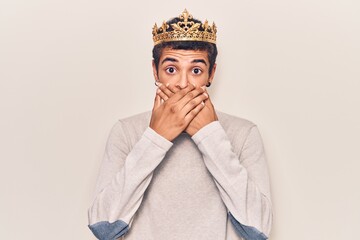 Young african amercian man wearing prince crown shocked covering mouth with hands for mistake. secret concept.