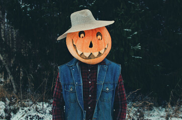 Halloween Scarecrow with a pumpkin orange on its head in a dark winter forest