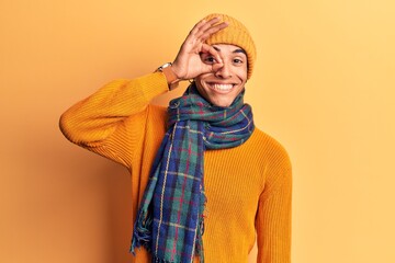 Young african amercian man wearing casual winter clothes smiling happy doing ok sign with hand on eye looking through fingers