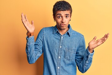 Young african amercian man wearing casual clothes clueless and confused with open arms, no idea and...