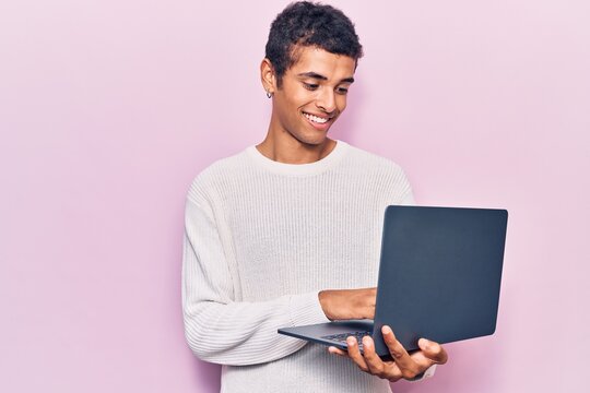 Young african amercian man holding laptop looking positive and happy standing and smiling with a confident smile showing teeth