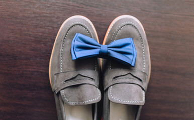 Wedding details, morning groom. Leather gray shoes and a blue bow tie lie on a background of brown floor close-up. Composition and concept.
