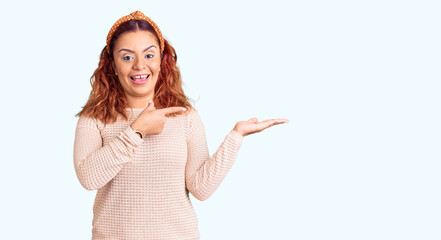 Young latin woman wearing casual clothes and diadem amazed and smiling to the camera while presenting with hand and pointing with finger.