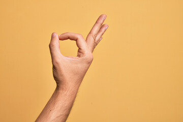 Hand of caucasian young man showing fingers over isolated yellow background gesturing approval expression doing okay symbol with fingers