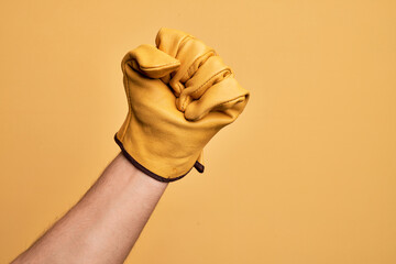 Hand of caucasian young man with gardener glove over isolated yellow background doing protest and...