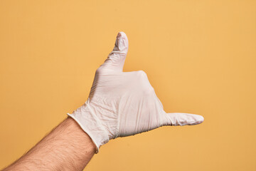 Hand of caucasian young man with medical glove over isolated yellow background gesturing Hawaiian shaka greeting gesture, telephone and communication symbol