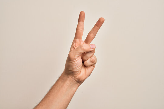 Hand of caucasian young man showing fingers over isolated white background counting number 2 showing two fingers, gesturing victory and winner symbol