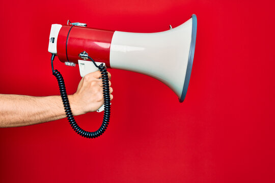 Beautiful hand of man holding megaphone over isolated red background