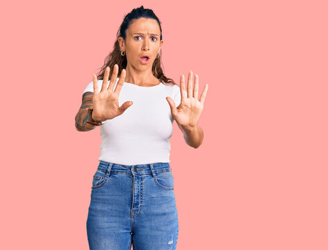 Young hispanic woman with tattoo wearing casual white tshirt doing stop gesture with hands palms, angry and frustration expression