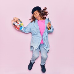 Young beautiful latin artist woman wearing french beret smiling happy. Jumping with smile on face painting using paintbrush and palette over isolated pink background