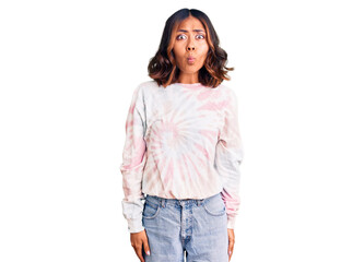 Young beautiful mixed race woman wearing casual tie dye sweatshirt making fish face with lips, crazy and comical gesture. funny expression.