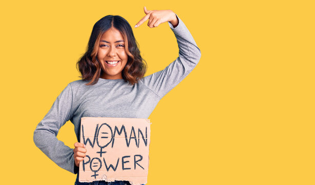 Young beautiful mixed race woman holding woman power banner pointing finger to one self smiling happy and proud