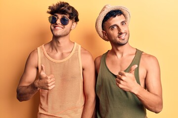 Young gay couple wearing summer clothes doing happy thumbs up gesture with hand. approving expression looking at the camera showing success.