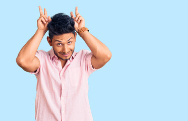 Naklejka premium Handsome latin american young man wearing casual summer shirt posing funny and crazy with fingers on head as bunny ears, smiling cheerful