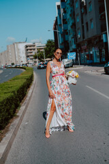 Young beautiful stylish caucasian woman model in summer dress with flower box in her hand on the street
