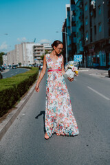 Young beautiful stylish caucasian woman model in summer dress with flower box in her hand on the street