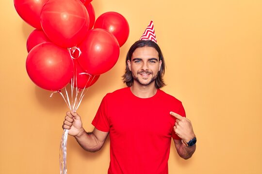 Young handsome man holding balloons pointing finger to one self smiling happy and proud