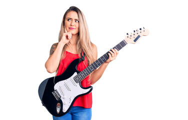 Fototapeta premium Young beautiful blonde woman playing electric guitar serious face thinking about question with hand on chin, thoughtful about confusing idea