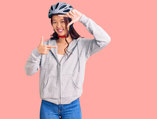 Young beautiful chinese girl wearing bike helmet smiling making frame with hands and fingers with happy face. creativity and photography concept.