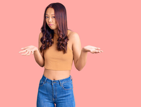 Young beautiful chinese girl wearing casual clothes clueless and confused expression with arms and hands raised. doubt concept.