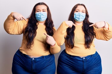 Young plus size twins wearing medical mask looking confident with smile on face, pointing oneself...