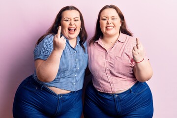 Young plus size twins wearing casual clothes showing middle finger doing fuck you bad expression, provocation and rude attitude. screaming excited