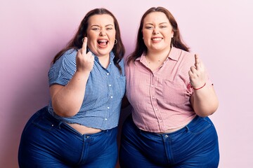 Young plus size twins wearing casual clothes showing middle finger doing fuck you bad expression,...