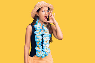 Young beautiful latin girl wearing hawaiian lei and summer hat shouting and screaming loud to side...