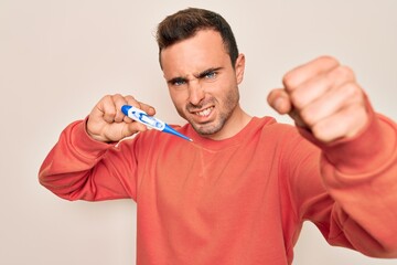 Young handsome man with blue eyes measuring temperature using digital thermometer annoyed and frustrated shouting with anger, yelling crazy with anger and hand raised