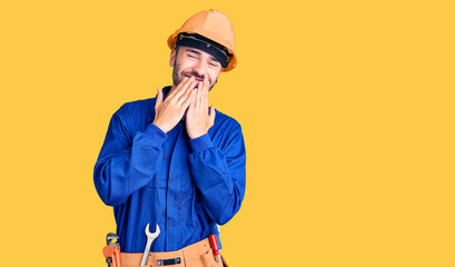 Young hispanic man wearing worker uniform laughing and embarrassed giggle covering mouth with hands, gossip and scandal concept