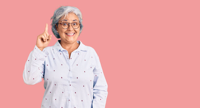 Senior woman with gray hair wearing casual business clothes and glasses pointing finger up with successful idea. exited and happy. number one.