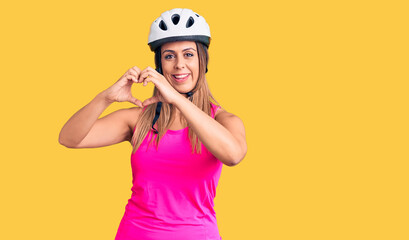 Young beautiful woman wearing bike helmet smiling in love showing heart symbol and shape with hands. romantic concept.